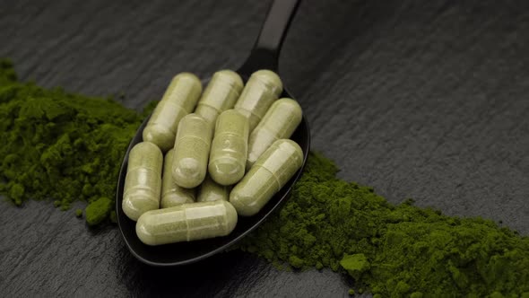 Superfoods capsule moringa or spirulina in black spoon and powder, rotating