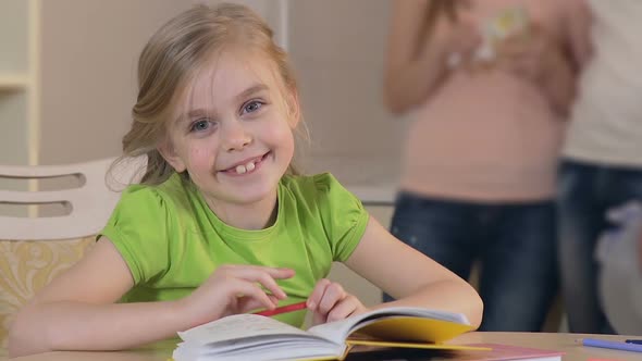 Pretty Little Girl Sitting at the Table and Looking Into Camera, Happy Family alt