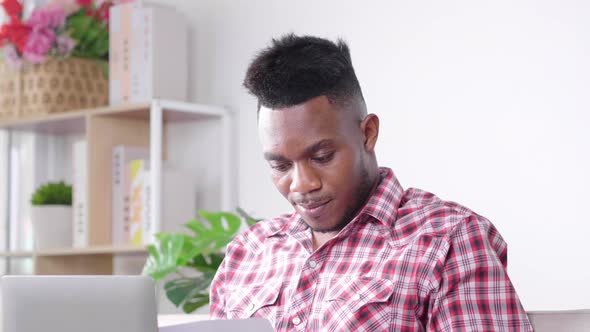 Busy African man working from home holding a lot of financial document, using laptop alt