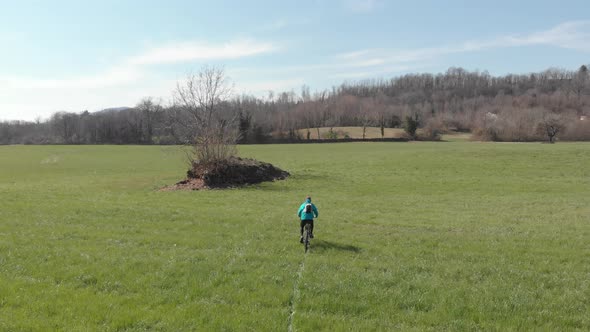 Aerial: man having fun by riding mountain bike in the grass on sunny day, scenic alpine landscape alt