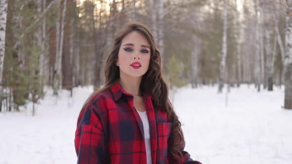 Young Woman with Wavy Hair Standing and Touching Face in Winter Forest