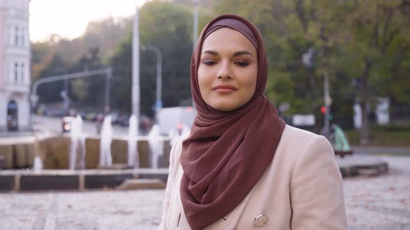 A Young Beautiful Muslim Woman Nods at the Camera with a Smile in a Street in an Urban Area alt