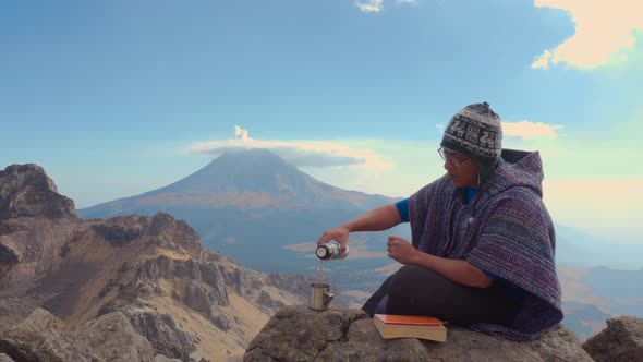 Man sitting outside on rocks  holding a book and looking the landscape alt