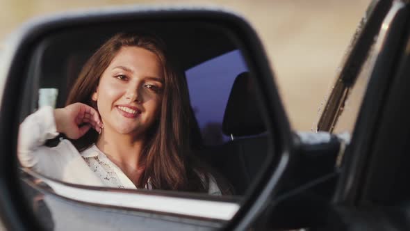 Woman in Car Looks Into Rear View Mirror and Smiling alt