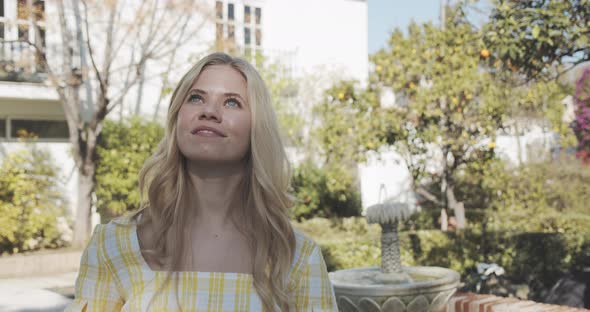 Woman in Garden Looking Up and Takes Photo of Sky with Fountain in Background alt