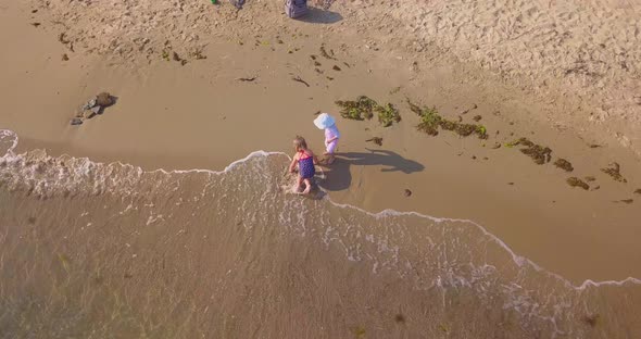 Drone Circling Video of Two Little Girls Plays in the Sand on the Sea Beach