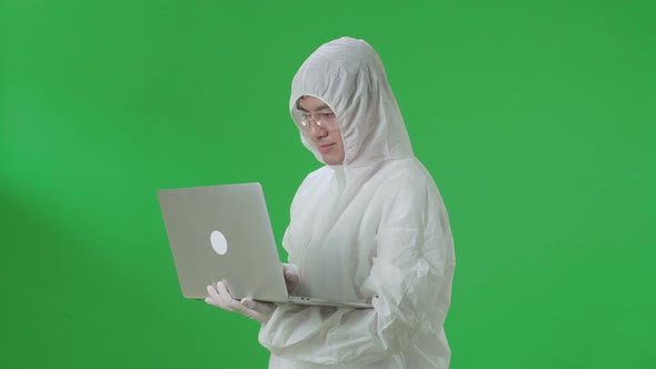 Side View Of Asian Man Wear Uniform Ppe Holding And Working With Laptop In The Green Screen Studio alt
