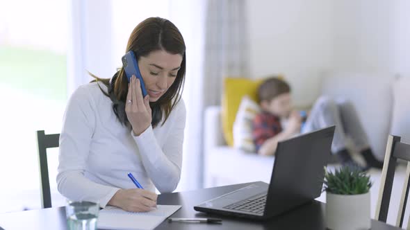 Single mother working at home office with son in background