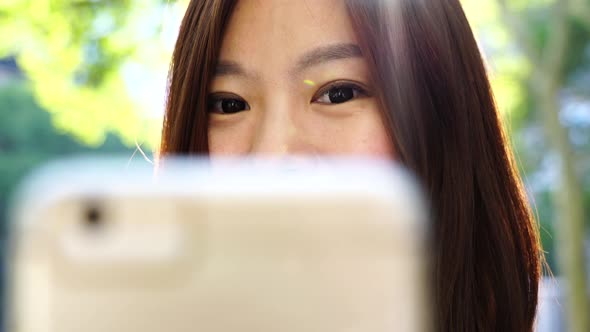 Beautiful Young Asian Female Browsing the Internet on Mobil Phone alt