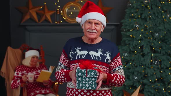 Elderly Grandfather in Festive Sweater Presenting Christmas Gift Box Smiling Looking at Camera alt