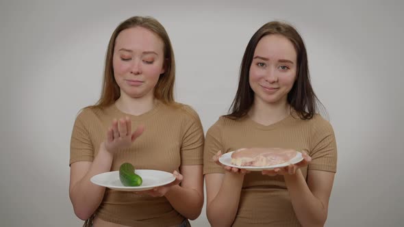 Twin Sisters Posing with Raw Meat and Fresh Organic Cucumber at Grey Background alt