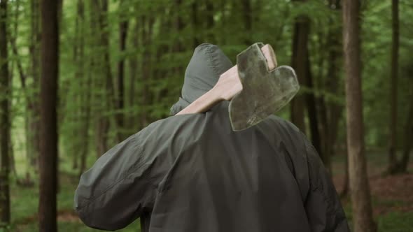 Professional Woodcutter Walking with Pro Ax in Wild Deciduous Forest. alt