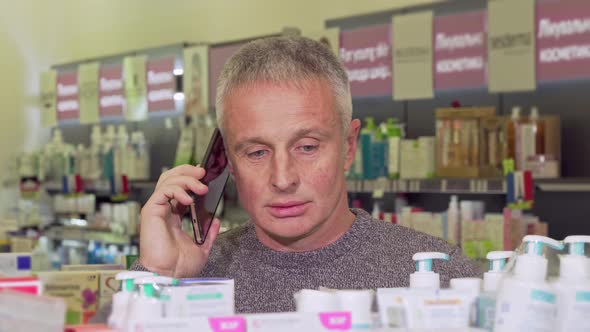 Senior Man Talking on the Phone, While Shopping at the Pharmacy alt