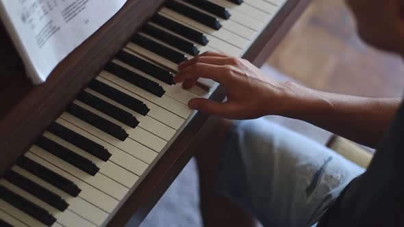 The hands of a young man take over the keys while playing the piano.