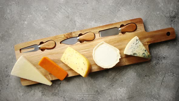Assortment of Various Kinds of Cheeses Served on Wooden Board with Fork and Knives alt