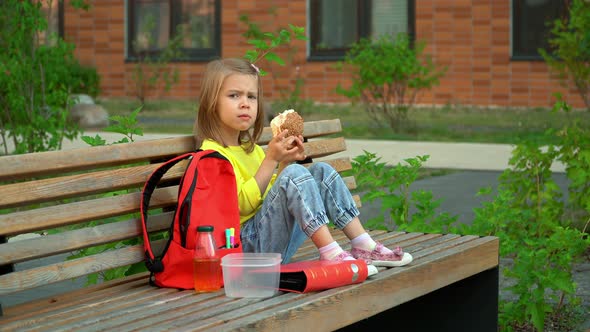 Girl Sits in Schoolyard and Eats Hamburger