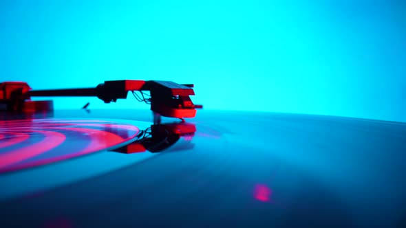 Black Vinyl Record Spinning and Play Music on Old Turntable in Rays of Bright Red and Blue Neon alt
