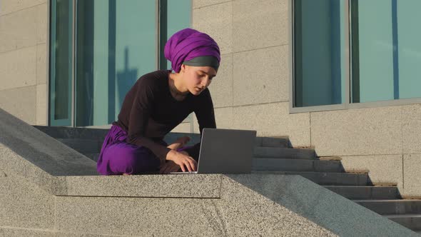 Islamic Muslim Business Woman Student User Sits Outdoors Background of City Building Working alt
