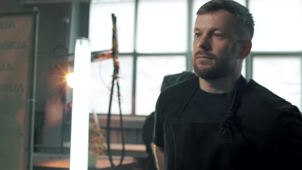 Professional worker in a private production facility goes to his machine and ties a protective apron