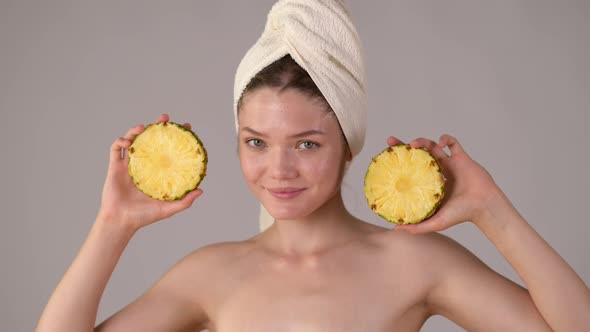 Young healthy smile woman with towel after shower holding juicy pineapple slices alt