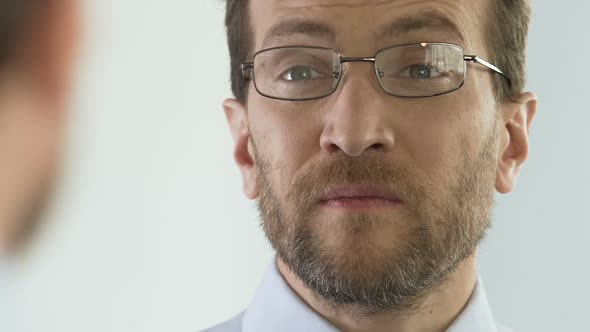 Male Wearing Eyeglasses and Frowning in Front of Mirror, Bad Eyesight Problem alt
