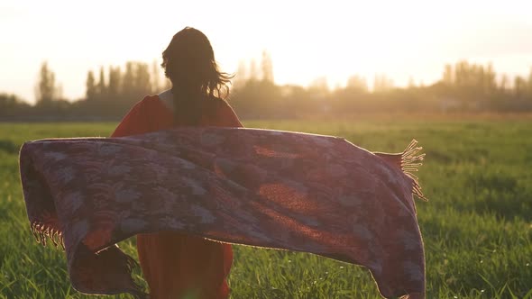 Beautiful Young Woman in a Red Dress Running in a Green Wheat Field at Sunset or Dawn alt