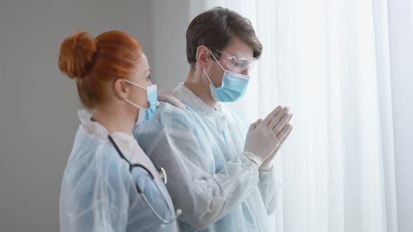 Side View of Empathic Nurse Supporting Doctor Praying Indoors alt