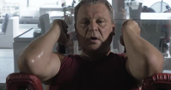 Man Getting Tired and Sweaty Training on Fitness Machine alt