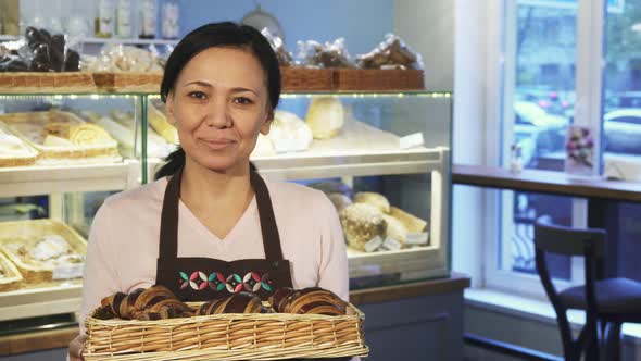 Mature Female Baker Posing at Her Store with a Basket Full of Croissants