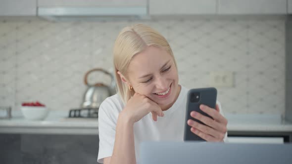 Cheerful Blonde Woman Actively Listens in Video Call While Sitting in Kitchen