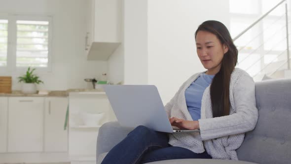 Happy asian woman sitting on sofa, resting with laptop at home alt
