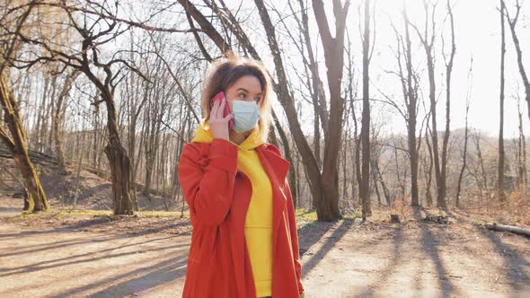 Attractive Woman Wearing Surgical Mask Talking on Mobile Phone Staying in the Park, Sunny Day