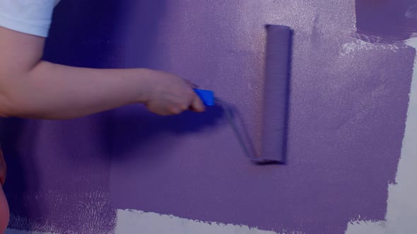 Close Up of Woman's Hand in Protective Glove Painting Wall in Purple Colour with Roller alt