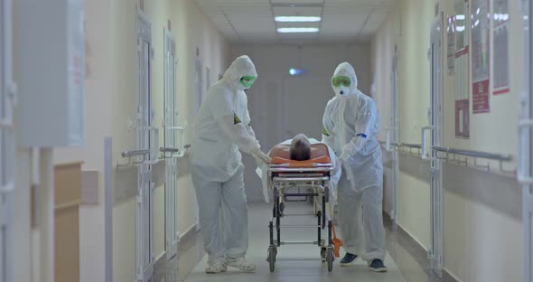 Doctors in Protective Suits and Masks Carry the Patient with a Coronavirus on a Stretcher to the alt