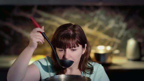 Happy Woman Tasting Soup on Spoon in Modern Kitchen and Smiling