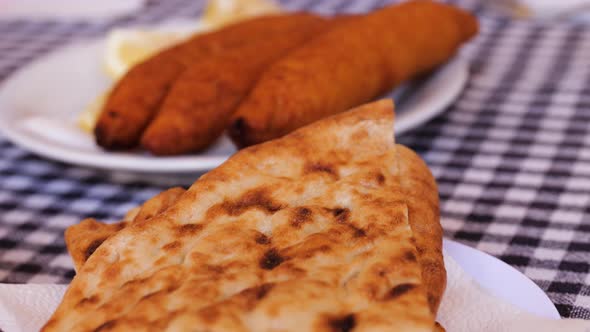 Close Up View Across Fresh Baked Flatbread Piled On Plate On Table Along With Other Dishes With Dips alt