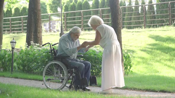 Caring Senior Woman Helping Handicapped Man To Stand Up From Wheelchair and Walk. Thankful Caucasian alt