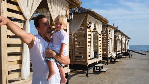 Dad Holds His Son in His Arms and Shows Him Something with a Finger in White Shirts alt