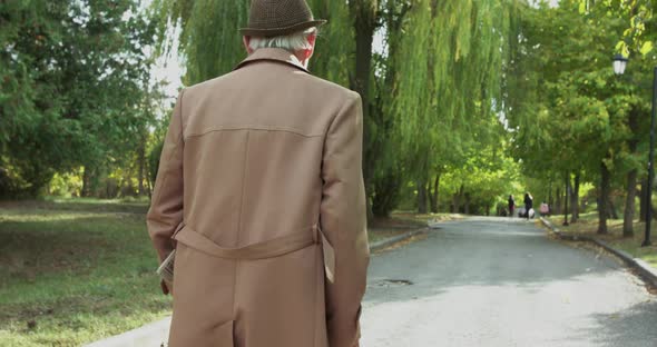 Back Look of Alone Grandfather in Outerwear Walking with Crutch Slowly on Square alt