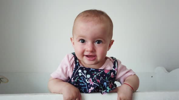 Cule baby laughing and having fun, standing in crib. Happy baby. Baby emotions. Baby smile. alt