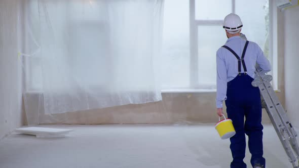 Man with Stepladder and Can of Paint in His Hands Prepares To Paint Walls During an Indoor alt
