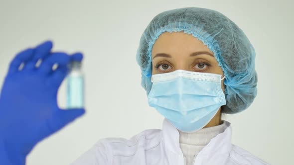 A Female Doctor in a Face Mask and in Medical Blue Gloves Shows a Ampoule with Coronavirus Vaccine alt
