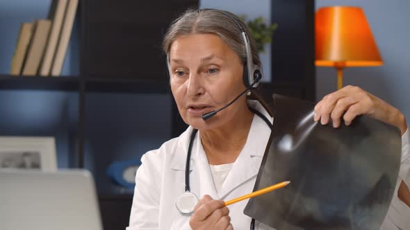 Aged Female Doctor Wearing Headset and Explaining X-ray To Patient Online alt