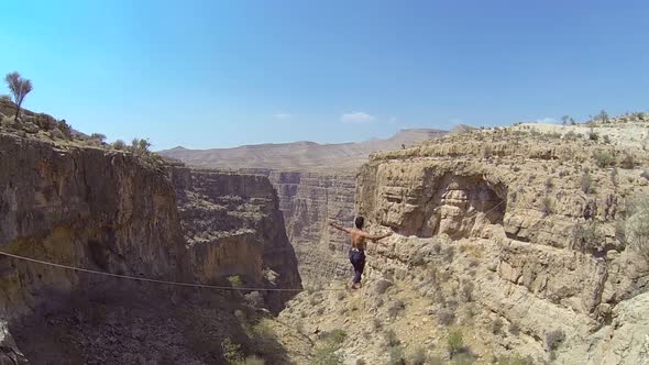 A man balances while tightrope walking and slacklining across a canyon alt
