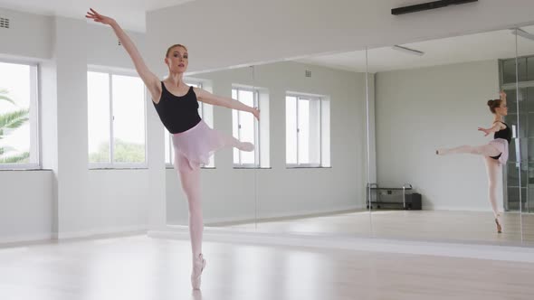 Caucasian female ballet dancer practicing ballet during a dance class in a bright studio alt