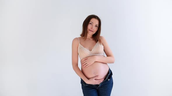 Stylish Pregnant Women in underwear and jeans Posing near the mirror on a white background. 
