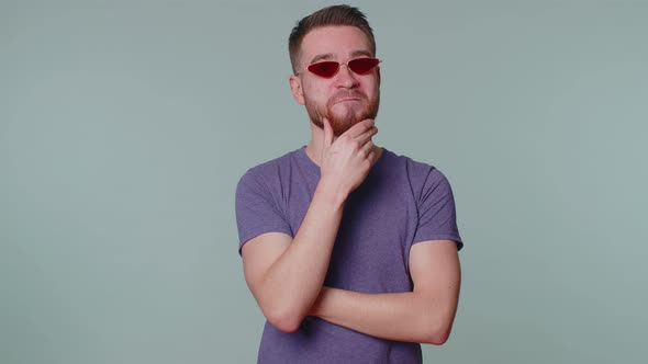 Seductive Cheerful Stylish Man in Purple Tshirt Wearing Sunglasses Charming Smile on Gray Wall alt