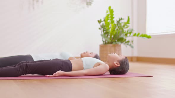 Asian little girl doing yoga dead body pose or nidra meditate with her mom on yoga may at cozy home. alt