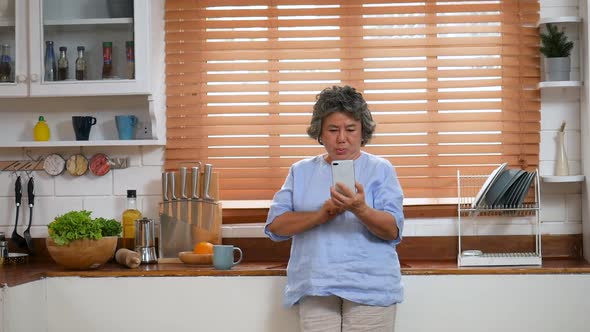 Portrait senior Asian woman using smartphone happy and smiling in the kitchen at home.