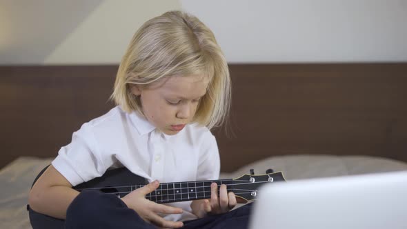 Distance Learning Online Education. A Preschool Boy Learning To Play the Ukulele on Laptop at Home